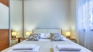 A neatly made bed with pillows, a bedside table with a lamp, and a mirror on the left side.