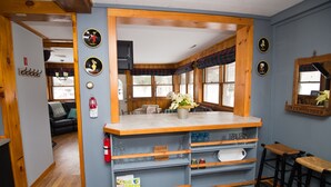 Una cocina con mostrador de madera, taburetes de bar y una ventana con cortinas escocesas.