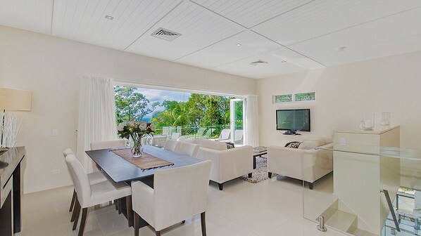 A modern living room with a dining area, a TV, and a glass cabinet.