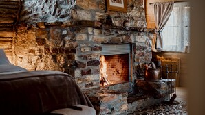 A cozy room with a stone fireplace, a bed with a cowhide rug, and a rustic wooden ceiling.