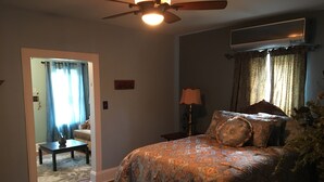 Ein Schlafzimmer mit einem großen Bett, Deckenventilator, Klimaanlage, Nachttisch, Lampe und einem Fenster mit Vorhängen.