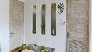 Een eetgedeelte met een houten tafel, stoelen en een plafondventilator. Drie verticale spiegels hangen aan de muur en er is een deur met een decoratieve knop.