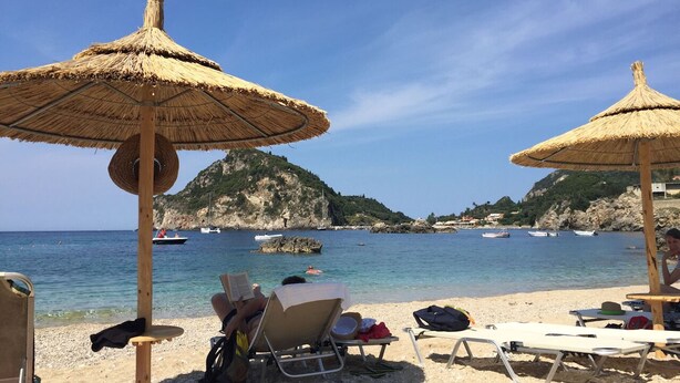 A beach with thatched umbrellas, lounge chairs, and a clear view of boats on the water.