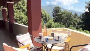 A terrace with a table set for two, surrounded by chairs, overlooking a mountainous landscape.