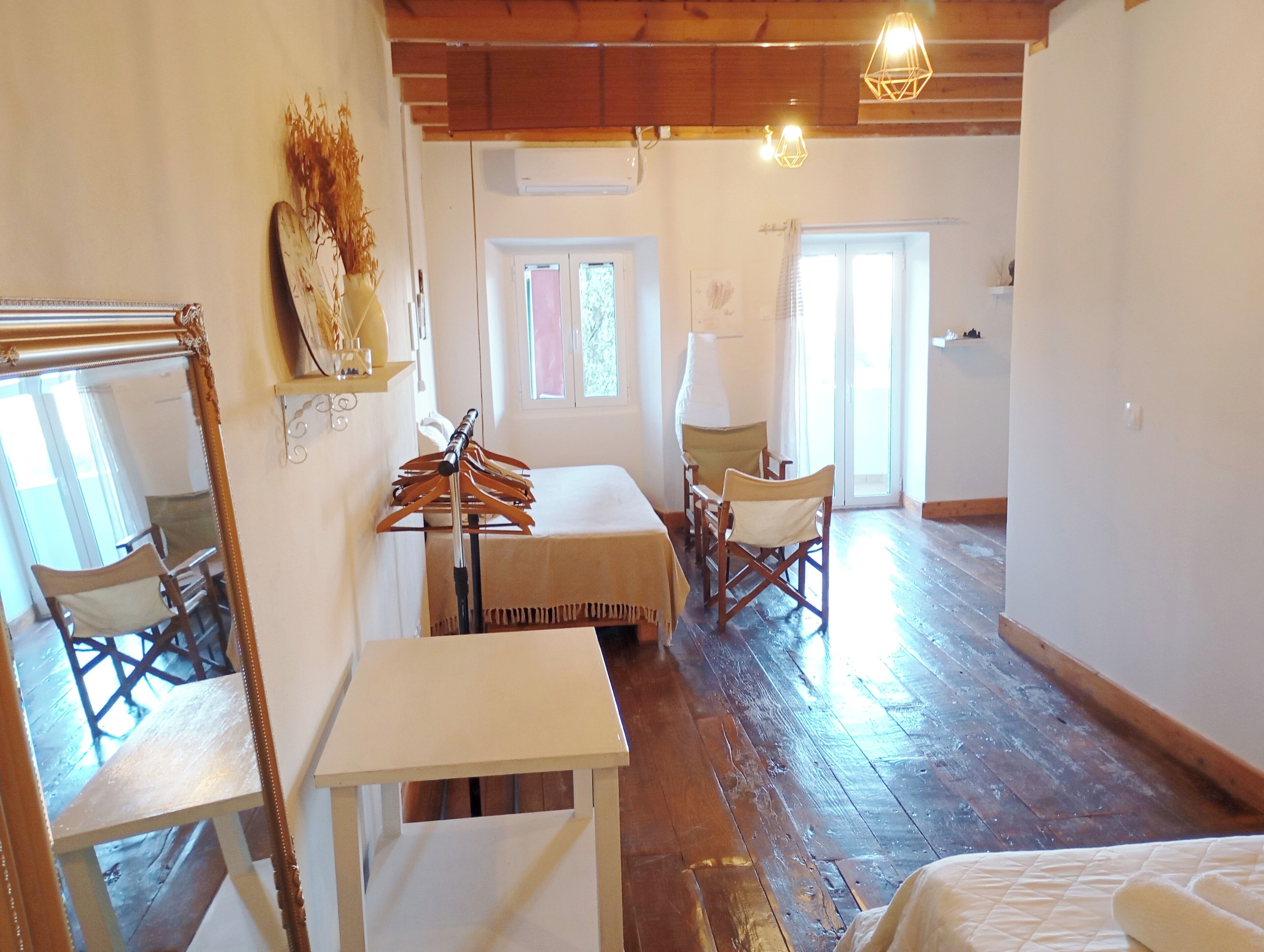 Habitación con piso de madera, una cama, una mesa y una silla. Tiene una ventana con cortinas y una puerta.