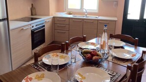 A compact kitchen with a stove, sink, and cabinets. There is a dining table with chairs and a fruit bowl.