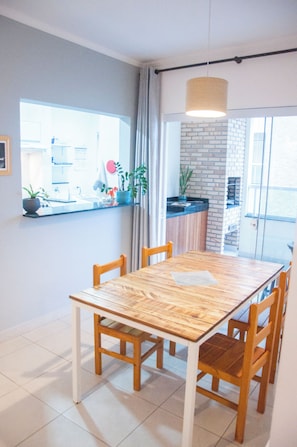 A dining area with a wooden table and chairs, a window with a view of the outside, and a brick wall.