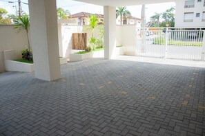 An open paved area with a white gate, concrete pillars, and potted plants.