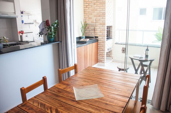 A wooden dining table with chairs, a kitchen area with a stove, and a view of the outside.
