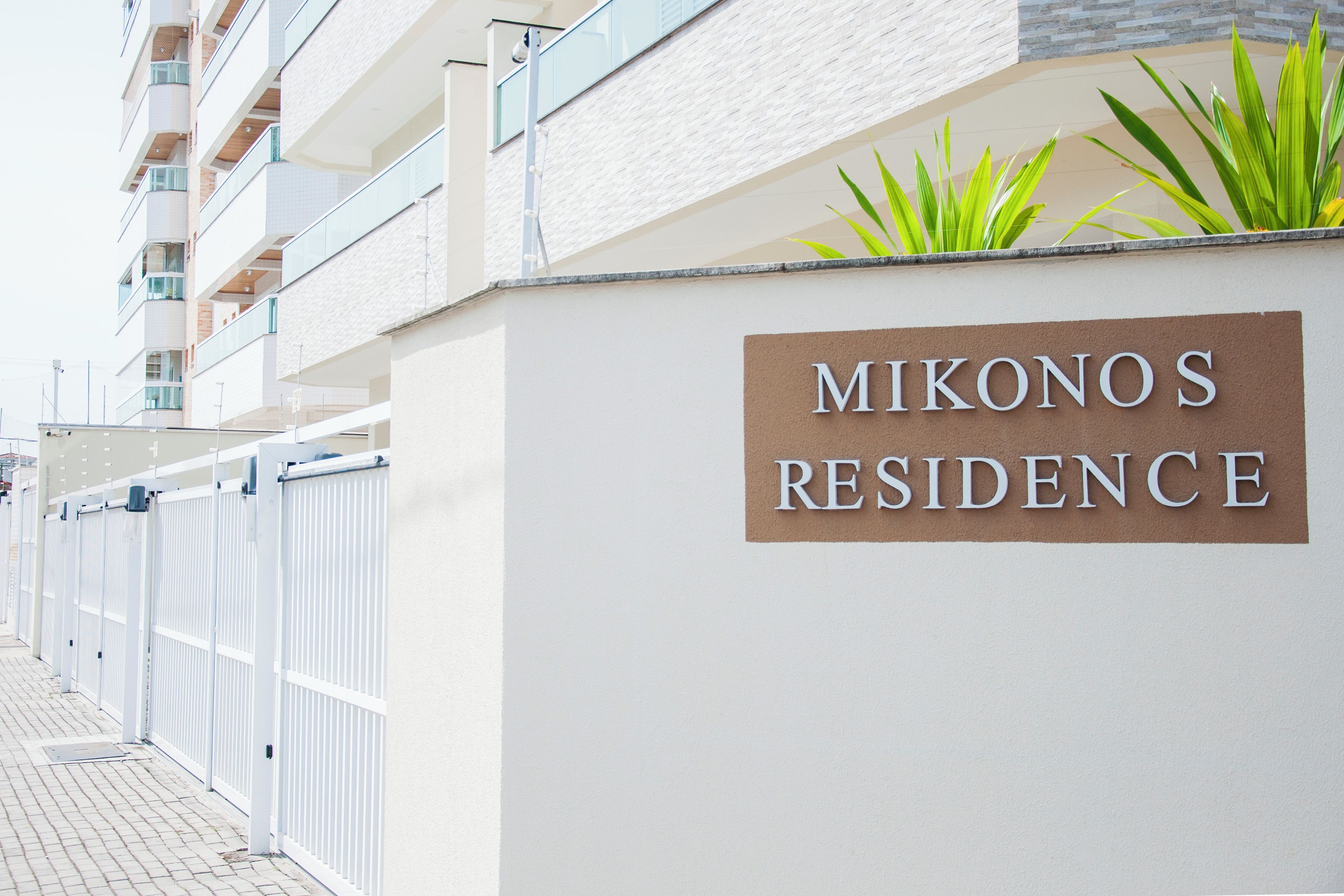 Senyal per a 'Mikonos Residence' amb un edifici modern al fons.