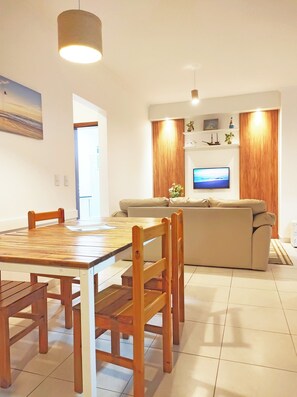 A modern living room with a dining table, chairs, a sofa, a television, and a wooden accent wall.