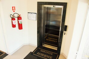 A hotel entrance with a glass door, fire extinguishers, and a welcome mat.