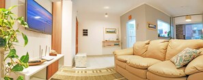 Un salon moderne avec un canapé beige, un téléviseur à écran plat, une petite table en bois et un coussin décoratif à motifs.
