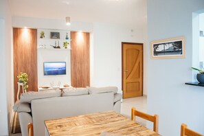 A modern living room with a sofa, a wooden dining table, and a television on the wall.