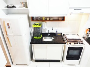 Een kleine keuken met een koelkast, spoelbak, fornuis en een plank met mokken.