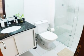 Un baño con inodoro blanco, lavamanos con encimera negra y mampara de ducha de vidrio.