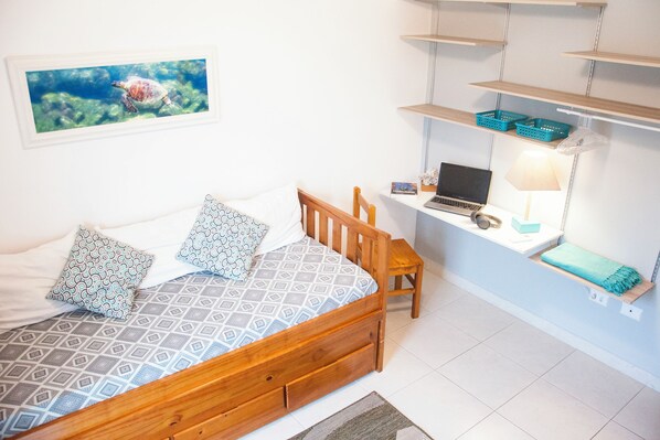 A bedroom with a bed, a desk, a laptop, and a shelf with items.