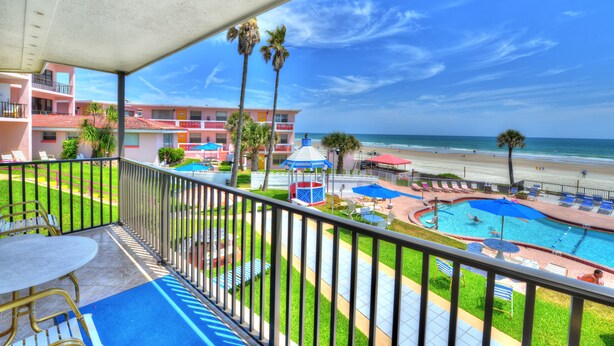 A balcony with a view of a beach, a swimming pool, and a building with a red roof. - Spacious 3 Bedrm/2 Bth OceanFront Apt w/Large Balcony Overlooking Pool. Sleeps 9 (Daytona Beach Shores)