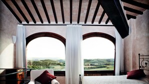 A bedroom with a bed, a chair, and two large windows with curtains.
