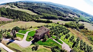 An aerial view of a historic building surrounded by lush green fields and forested hills.