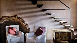 A modern interior with a staircase, white armchairs, and a rustic wooden box.