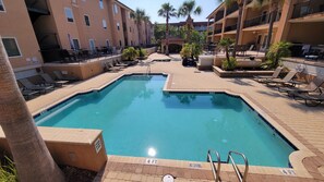 A hotel pool area with a 4 FT deep pool, lounge chairs, palm trees, and a covered seating area.