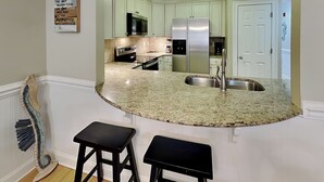 A kitchen with a curved granite countertop, stainless steel appliances, and a white door in the background.