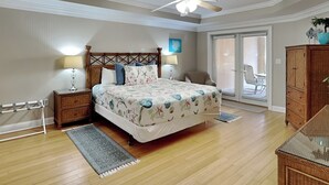A bedroom with a bed, two bedside tables, a ceiling fan, a chair, a wardrobe, and a view of the outside.
