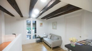 Una sala de estar moderna con vigas de madera a la vista, un sofá gris, una mesita con un florero y una ventana con vistas al exterior.