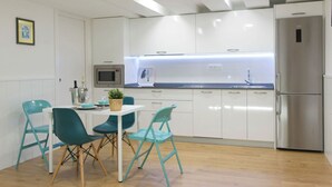 Una cocina moderna con armarios blancos, un refrigerador de acero inoxidable y sillas color turquesa alrededor de una mesa blanca.