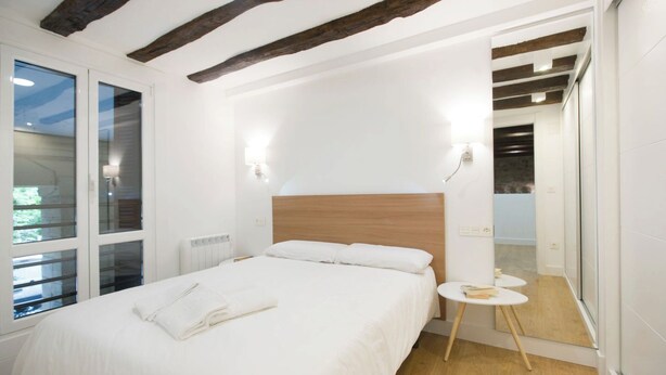 Un dormitorio moderno con una cama grande, vigas de madera, una mesita redonda y un vestidor.