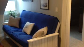A blue sofa with white cushions in a room with a radiator, a window with a view, and framed pictures on the wall.