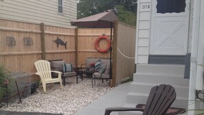 A backyard with a patio area, a wooden fence, and a sign indicating 'Beach Cottage'. - Cozy Beach Apartment, private entrance and parking spot . <br> (Middletown)