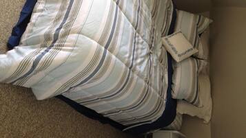 Ein Bett mit gestreifter Bettwäsche und einem Kopfkissen mit floralem Muster.
