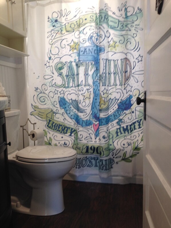 Un baño con inodoro, cortina de ducha con texto y diseños decorativos, y piso de madera.