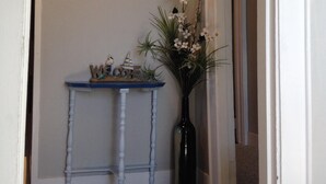 A hallway with a clock on the wall, a small table with decorative items, and a vase with flowers. - Cozy Beach Apartment, private entrance and parking spot . <br> (Middletown)