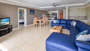 A modern living room with a blue sectional sofa, a wooden coffee table, and a TV. - Blue Water Views 9, Seaview Apartment on Hamilton Island (Hamilton Island)