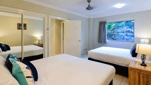 A hotel room with two beds, a mirror, a window with a view of trees, and a ceiling fan. - Blue Water Views 9, Seaview Apartment on Hamilton Island (Hamilton Island)