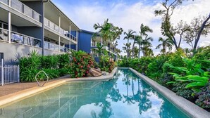 A swimming pool surrounded by lush greenery and a multi-story building with balconies. - Blue Water Views 9, Seaview Apartment on Hamilton Island (Hamilton Island)