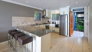 A modern kitchen with a central island, bar stools, stainless steel appliances, and a view of the garden. - Blue Water Views 9, Seaview Apartment on Hamilton Island (Hamilton Island)
