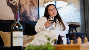 A person sitting on a couch with a wine bottle and chess pieces on a table.