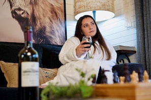 Una persona sentada en un sofá con una botella de vino y piezas de ajedrez sobre una mesa.