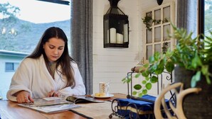A person reading a book at a wooden table with a small plant, a lantern, and a cup on the table.