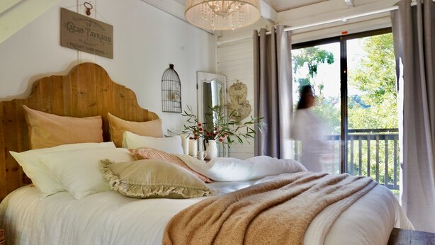 A bedroom with a wooden headboard, a large bed with multiple pillows, a vase with flowers, and a view of the outdoors through a sliding door.