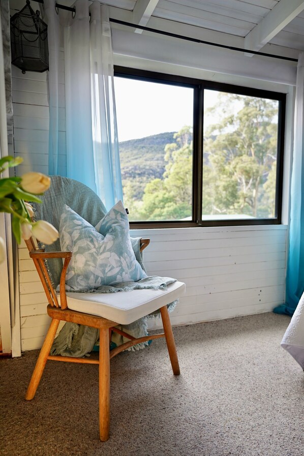 A cozy room with a wooden rocking chair, a large window with a view of trees and hills, and a hanging lantern. - Cedar Country Retreat - Country style luxury (Halls Gap)