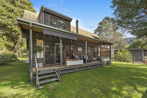 Ein zweistöckiges Haus mit verdeckter Veranda, großen Fenstern und einem gepflegten Rasen.