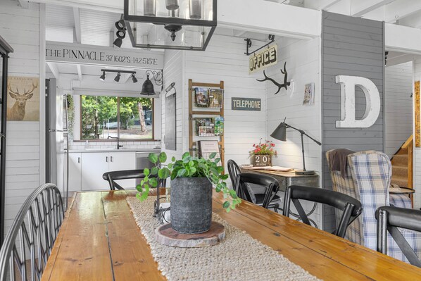 A dining area with a wooden table, chairs, a potted plant, and a view of the outside.