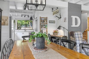 A dining area with a wooden table, chairs, a potted plant, and a view of the outside. - Cedar Country Retreat - Country style luxury (Halls Gap)