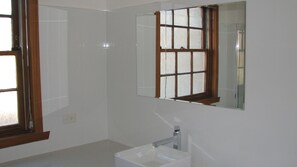 Une salle de bain avec un grand miroir, un lavabo et une fenêtre aux cadres en bois.