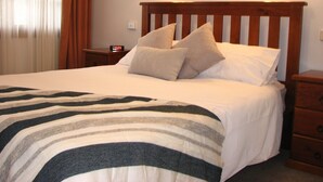A neatly made bed with a striped blanket, a wooden headboard, and two bedside lamps. - API Leisure & Lifestyle Battery Point (Battery Point)